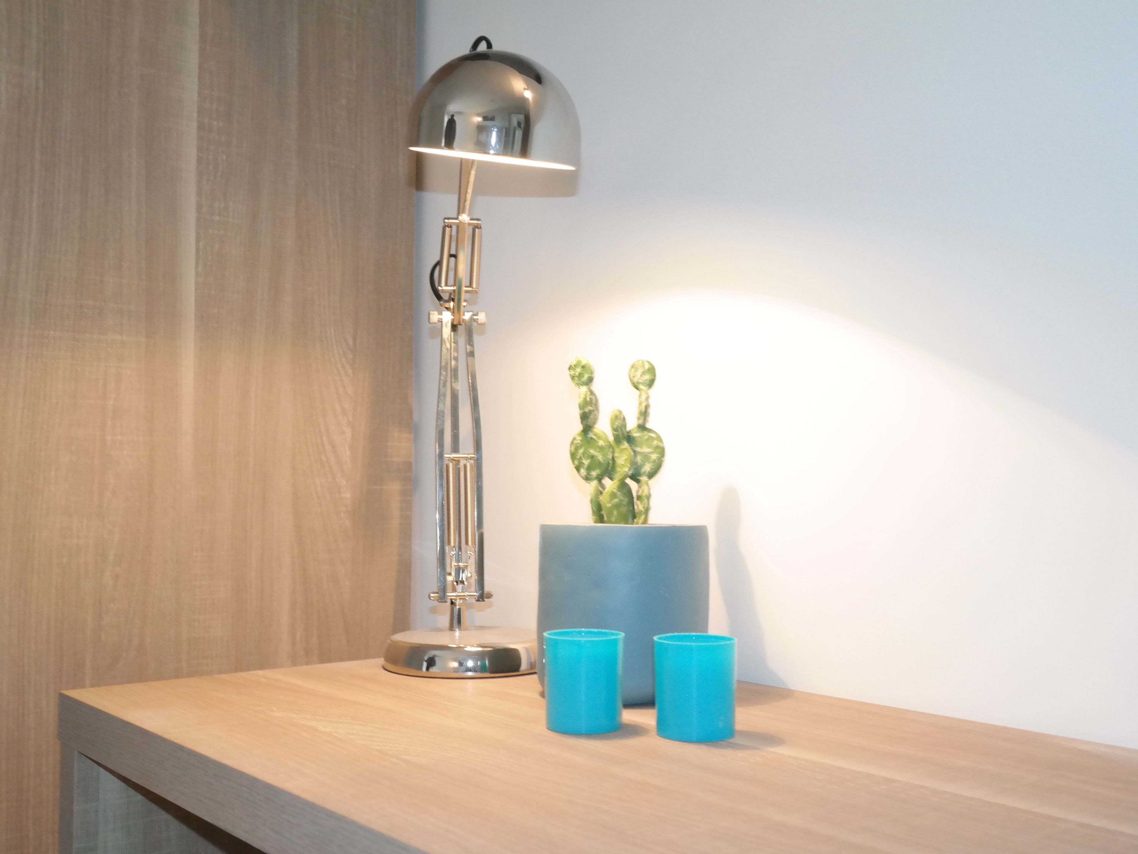 A desk with a floor lamp, a cactus plant, and two blue cups.