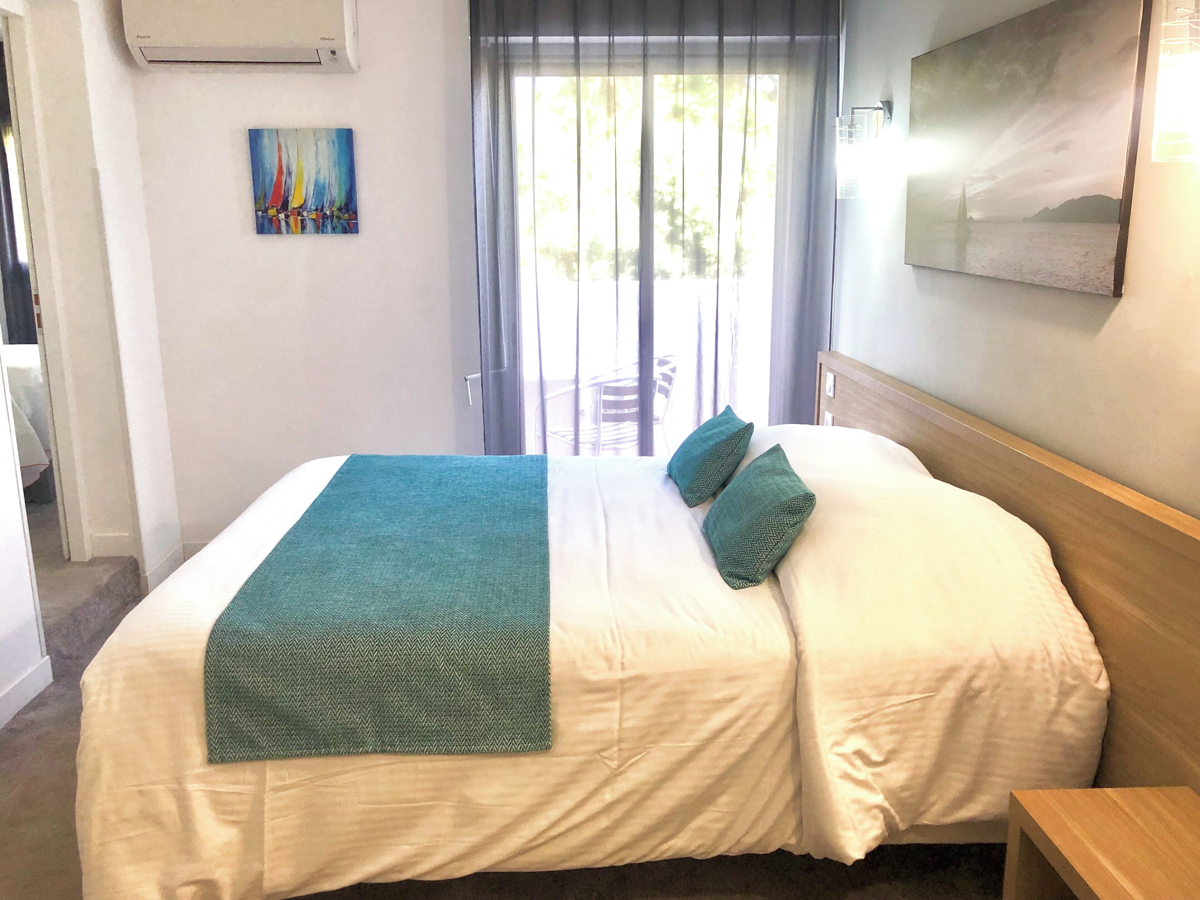 A hotel room with a bed, a painting on the wall, and a window with curtains.