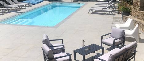 A pool area with lounge chairs, a table, and a covered seating area.