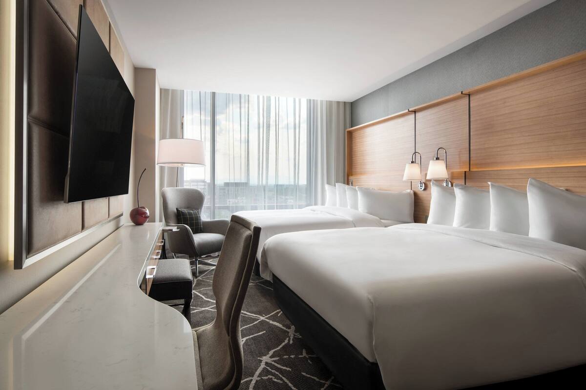 A hotel room with two beds, a flat-screen TV, a desk, a chair, and a lamp.