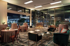 A modern hotel lobby with round tables, comfortable seating, and large windows offering city views.