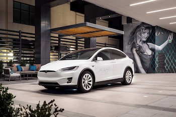 Experience the sleek Tesla Model 3 in a stylish showroom setting, surrounded by a contemporary mural and comfortable seating. at The Jacquard, Autograph Collection