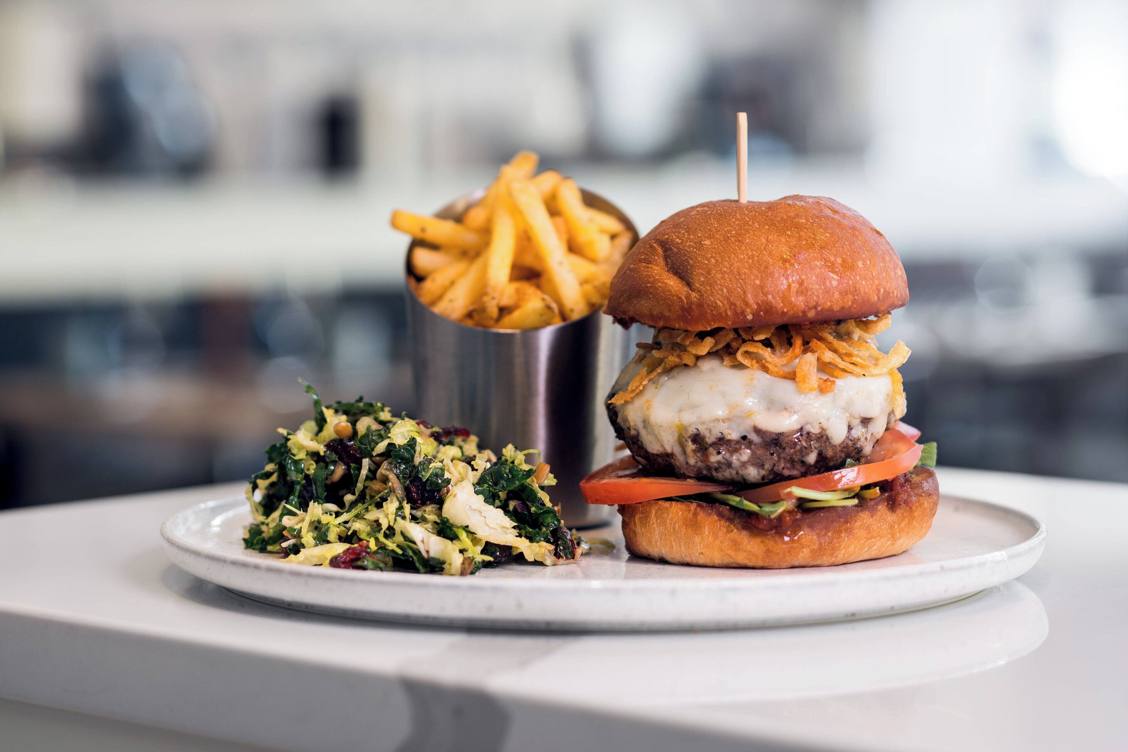 Hamburguesa con papas fritas y una ensalada pequeña en un plato blanco.