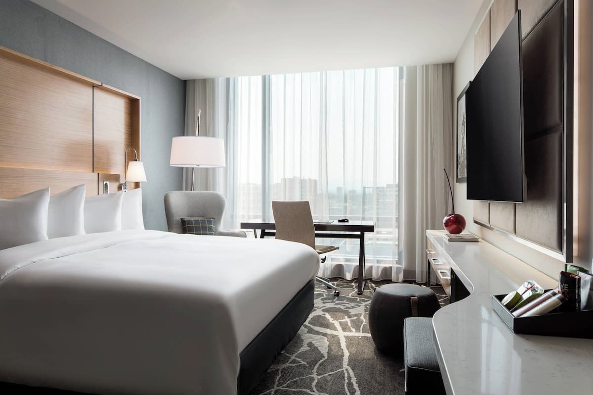 A modern hotel room with a large bed, a desk, a chair, and a TV.
