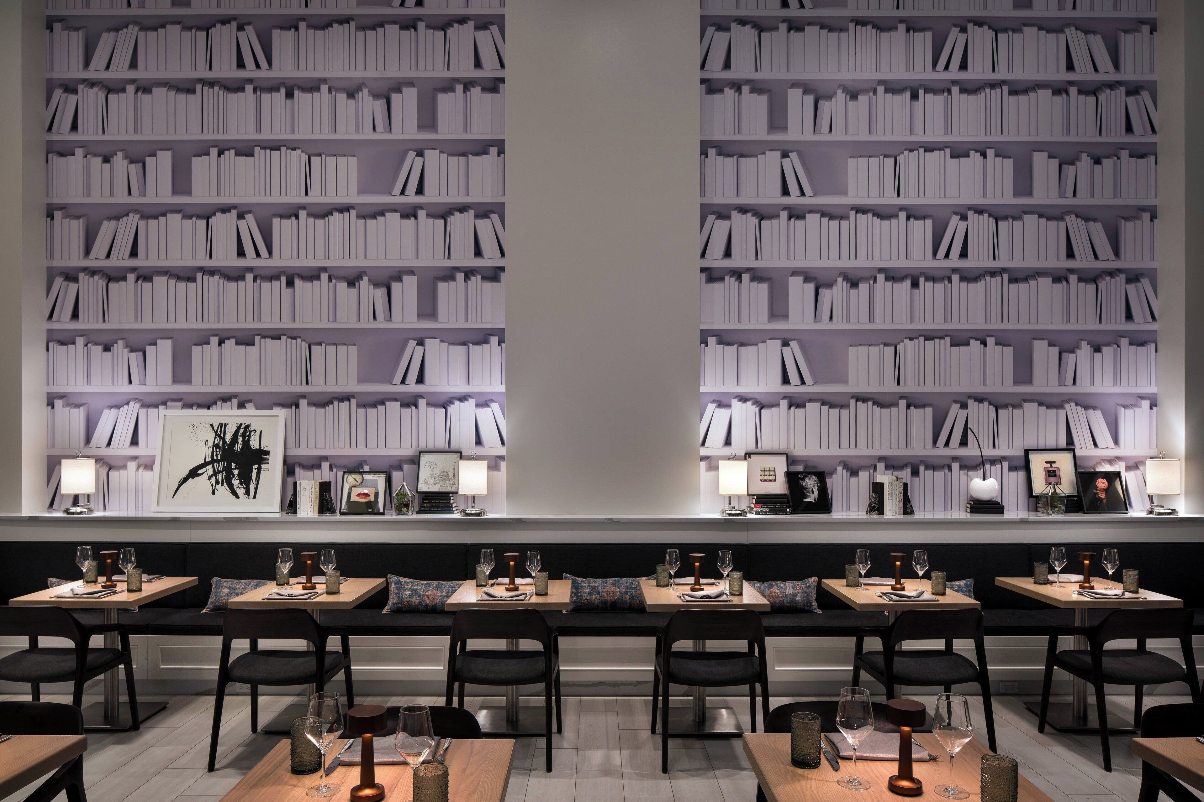 Un restaurant avec plusieurs tables, des chaises noires et une bibliothèque remplie de livres.