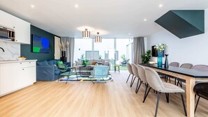 A modern apartment with a kitchen, dining area, and living room. It features a large window, a dining table with chairs, a sofa, and a coffee table. - Sweett | Brune II - Four Bedroom Apartment, Sleeps 10 (Paris)