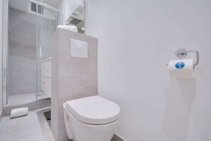 Ett modernt badrum med en toalett, en duschkabin med glasväggar och en handduksdispenser.