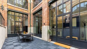 A modern building with large windows, a brick facade, and a patio area with a table and chairs. - Sweett | Brune VI - Three Bedroom Apartment, Sleeps 8 (Paris)
