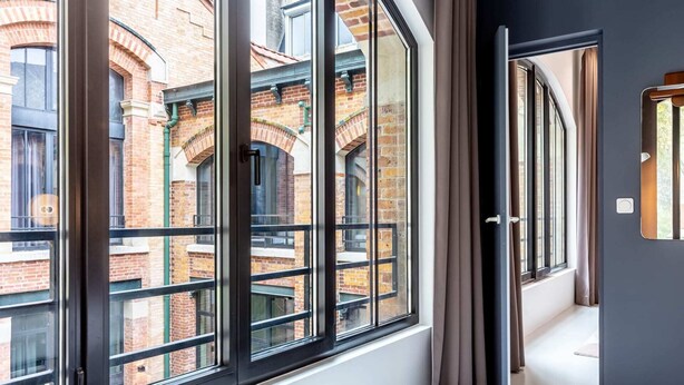 A room with large windows, a view of a brick building, and a door with a handle. - Sweett | Brune VI - Three Bedroom Apartment, Sleeps 8 (Paris)