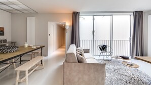 A modern living room with a sofa, a dining table, and a small balcony with a chair.