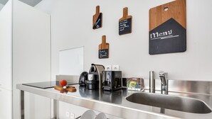 A modern kitchen with a stainless steel sink, a coffee machine, and a kettle. There are wooden cutting boards and a chalkboard menu on the wall.