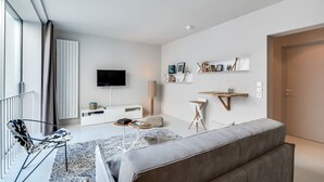 A modern living room with a grey sofa, a flat-screen TV, a white console table, and a bookshelf with books and decorative items.