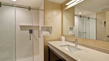 A modern bathroom with a glass-enclosed shower, a large mirror, and a vanity with a sink and towel rack.