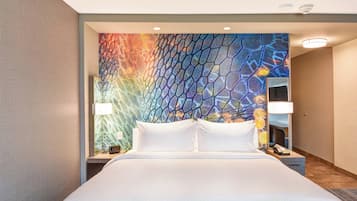 A hotel room with a large bed, two bedside tables, a nightstand, a mirror, and a colorful abstract wall design.