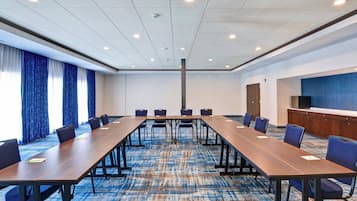 A conference room with a long table, chairs, a blue carpet, and a television on a cabinet.