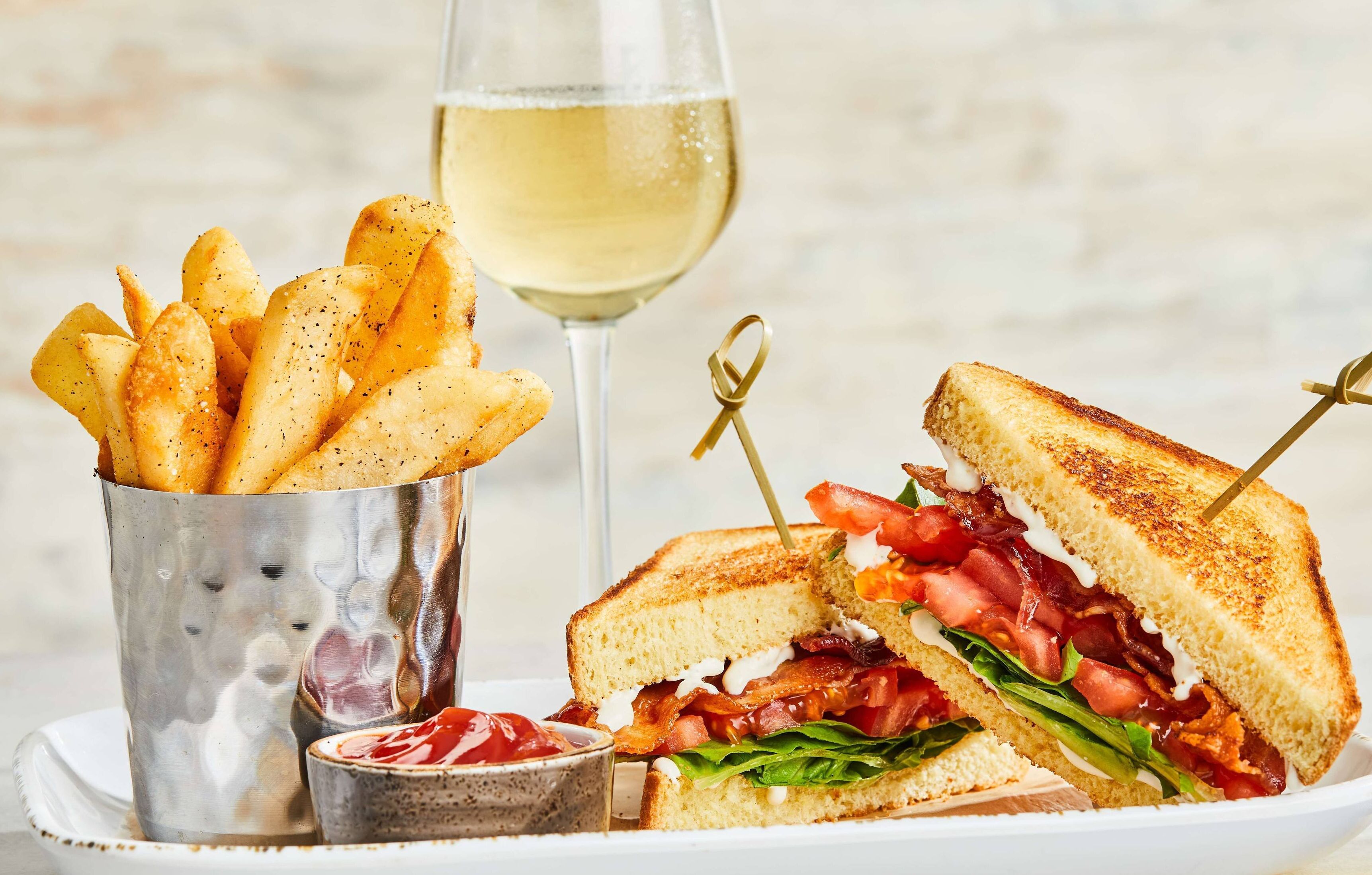 Ein Sandwich mit Pommes und einem Glas Weißwein.