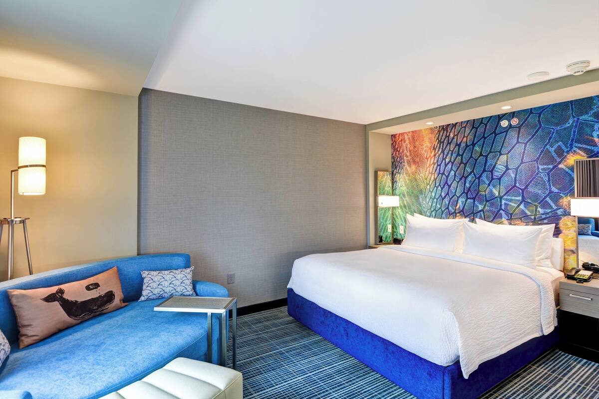 A hotel room with a bed, a blue sofa, a small table, and a colorful wall mural.