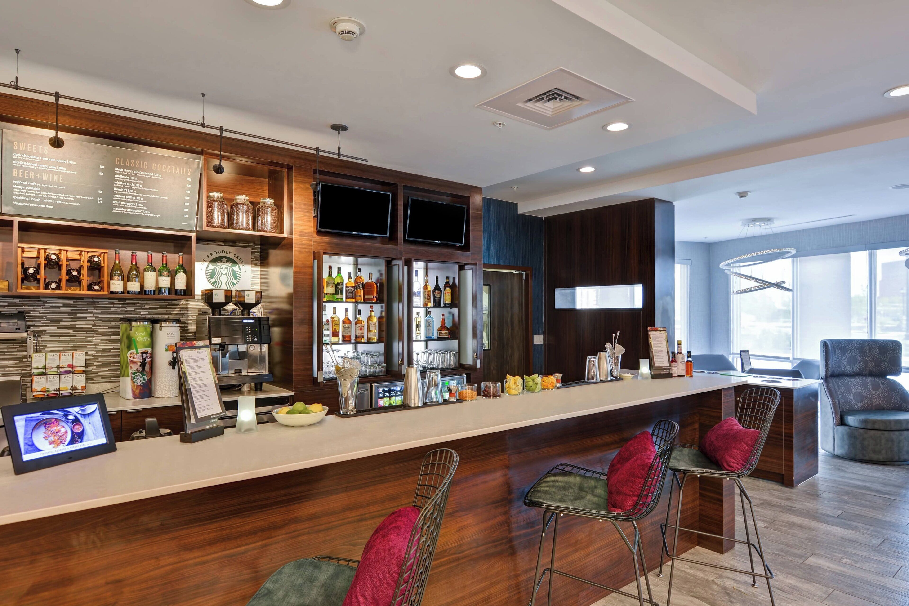 Un bar moderno con una barra larga, diversas opciones de asientos y una variedad de bebidas y alimentos exhibidos.
