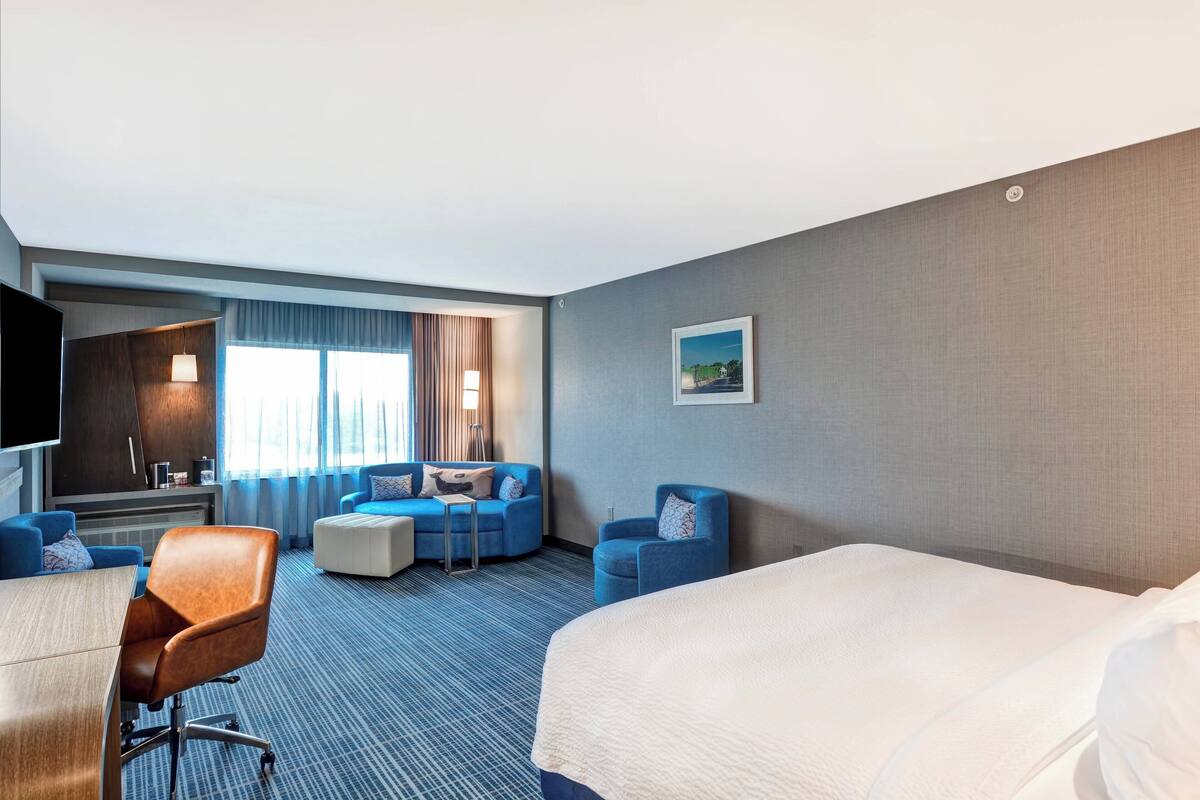 A hotel room with a large bed, a desk with a chair, a sofa, and a TV.