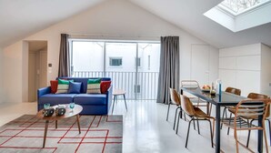 A modern living room with a blue sofa, a dining table with chairs, and a skylight. - Sweett | Brune IX - Two Bedroom Apartment, Sleeps 6 (Paris)