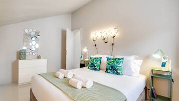 Un dormitorio ordenado con cama, almohadas, una mesita de noche, una lámpara y un espejo fijado a la pared.