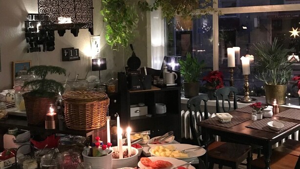 A dining area with a large window, a hanging lantern, and various food items on the table. - Hotel Lilton (Angelholm)