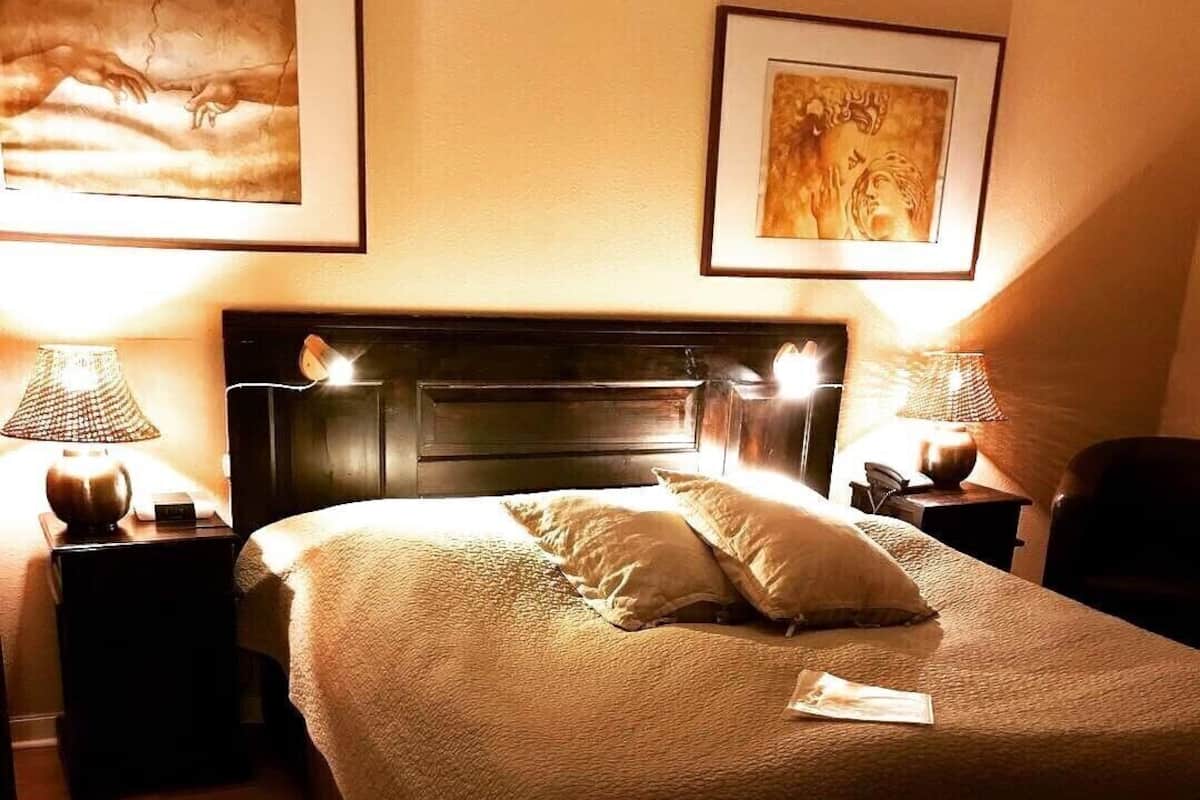 A neatly made bed with a headboard, two bedside tables with lamps, and artwork on the walls.