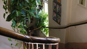 A staircase with ornate metal railings, a potted plant, and a bulletin board with various notices. - Hotel Lilton (Angelholm)