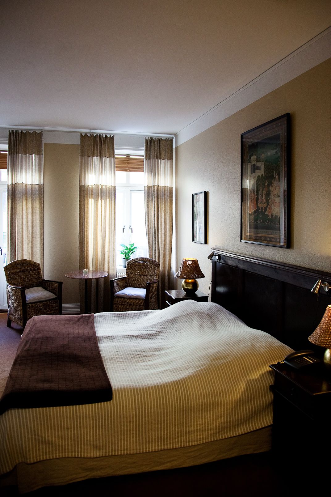 Une chambre d’hôtel avec un grand lit, deux chaises, une petite table, une lampe et un tableau au mur.