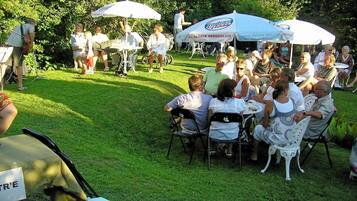 An outdoor gathering with people seated at tables under umbrellas, surrounded by greenery.