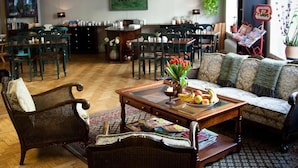A spacious living area with a wooden floor, a sofa, a coffee table with fruits and magazines, and a dining area in the background. - Hotel Lilton (Angelholm)