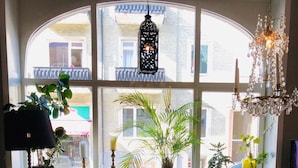 A cozy living room with a large arched window, a chandelier, and various plants and books. - Hotel Lilton (Angelholm)
