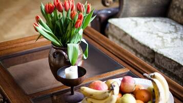 A wooden coffee table with a glass top, a vase of red tulips, and a plate of fruit.