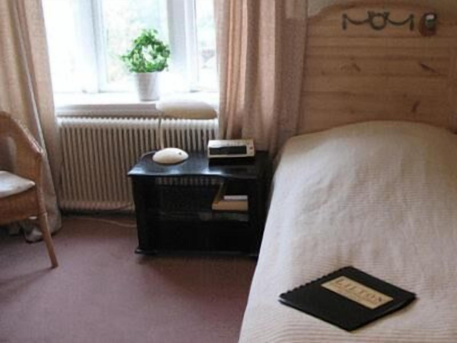 Un dormitorio con una cama, una mesita de noche con lámpara, una silla y una ventana con cortinas.