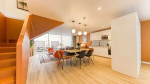 A modern apartment with a wooden staircase, a dining area with a table and chairs, a kitchen with white cabinets, and a large window overlooking a garden. - Sweett | Brune I - Two Bedroom Apartment, Sleeps 6 (Paris)