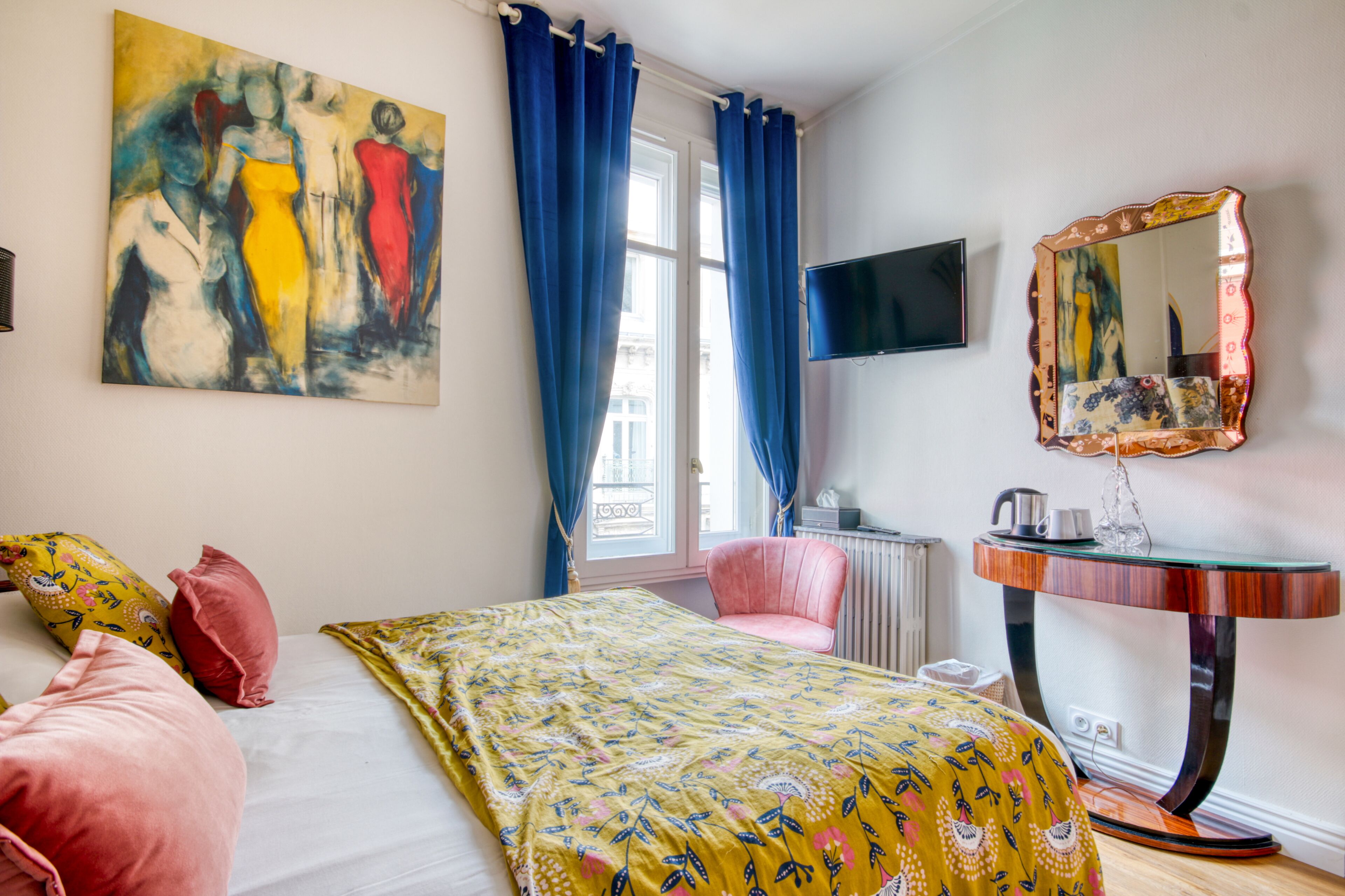 Une chambre à coucher avec un lit, une chaise rose, une table de chevet, un miroir et un tableau accroché au mur.