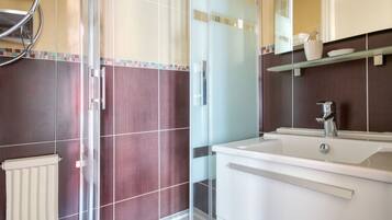 A bathroom with a glass shower enclosure, a white sink, and a mirror above the sink.