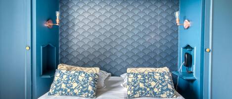Ein Bett mit zwei Kissen, ein Kopfteil mit geschwungener Musterung und ein Telefon an einer blauen Wand.
