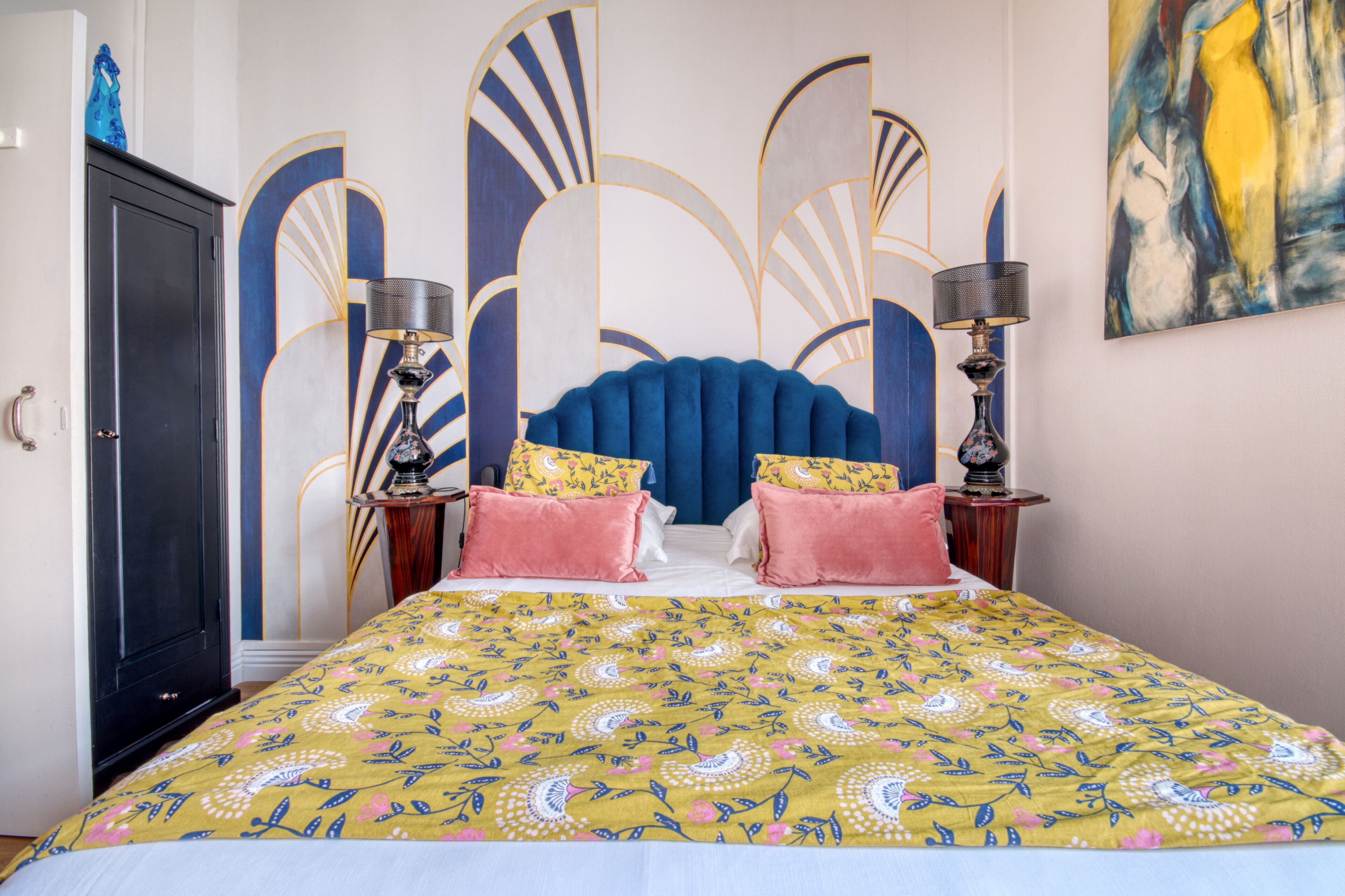 A bedroom with a bed, two bedside tables, a wardrobe, and a large abstract painting on the wall.