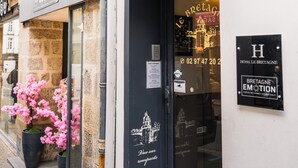 A hotel entrance with a sign reading 'HOTEL Le Bretagne,' a balcony with wrought iron railings, and a window displaying pink flowers. - Hôtel Le Bretagne (Vannes)