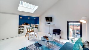 Un espacio habitable moderno con tragaluces, un comedor, un televisor montado en un estante blanco y vistas al exterior a través de una puerta de cristal.