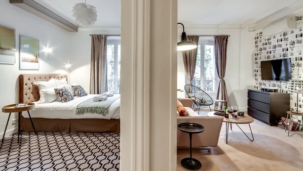 A modern bedroom with a large bed, a sofa, a dining table, and a TV. - Sweett | Saint Germain I (Paris)