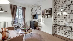 A modern living room with a large window, a flat-screen TV, and a wall decorated with camera prints. - Sweett | Saint Germain I (Paris)
