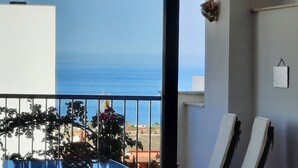 Een balkon met uitzicht op zee, een bloempot en een witte muur met een klein fotolijstje.