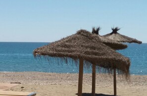 Una playa con sombrillas de paja y una vista despejada del mar.
