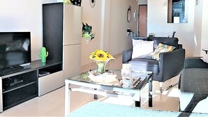 Een moderne woonkamer met een flatscreen televisie, een glazen salontafel, een bank en een divan.