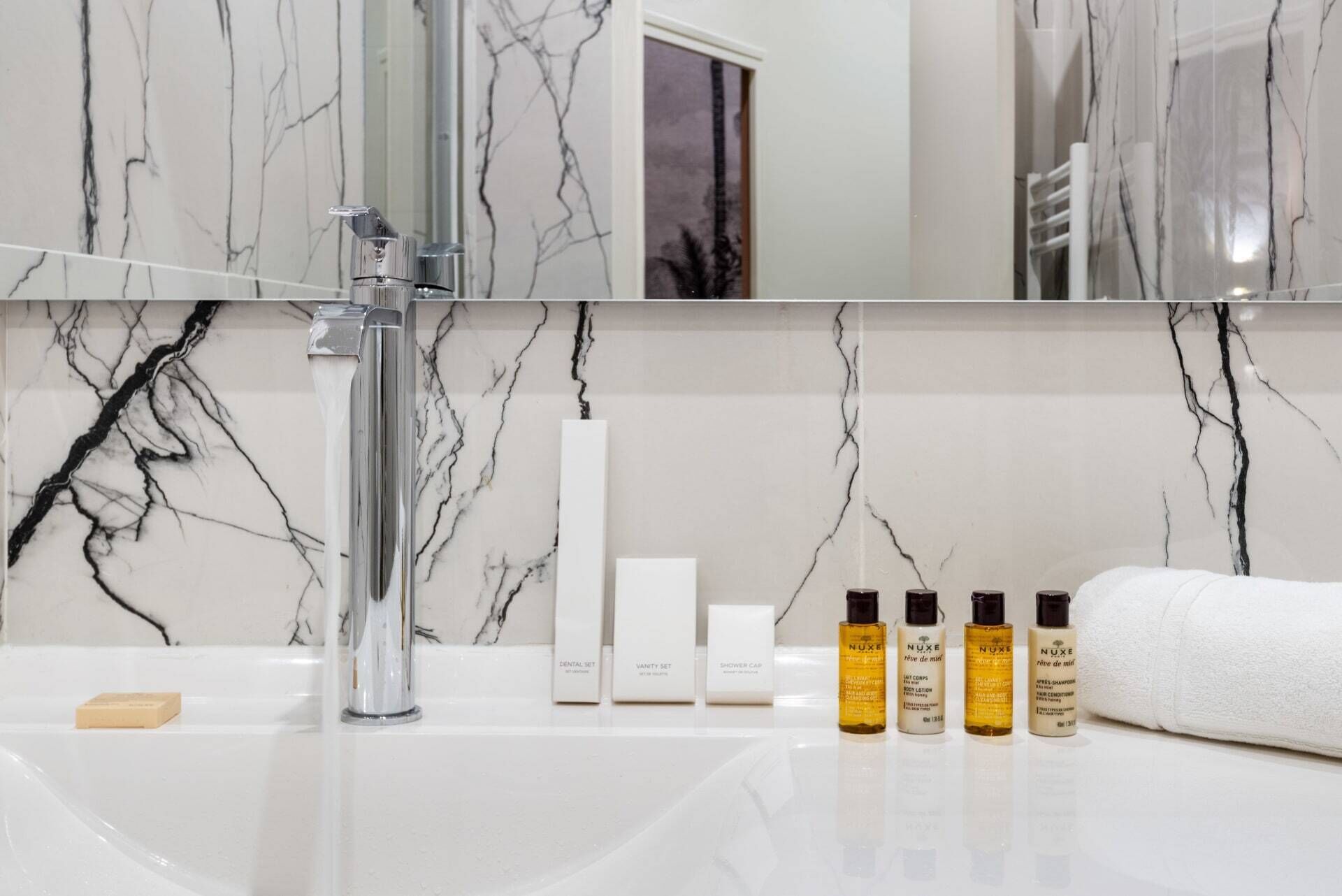 A bathroom with a marble sink, a modern faucet, and a mirror above. There are toiletries including a toothbrush, a soap bar, and three bottles of shampoo.
