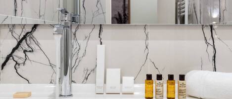 A bathroom with a marble sink, a modern faucet, and a mirror above. There are toiletries including a toothbrush, a soap bar, and three bottles of shampoo.