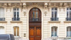 A building with a large wooden double door, ornate architectural details, and a balcony with wrought iron railings. - Sweett | Artois - Three Bedroom Apartment, Sleeps 6 (Paris)