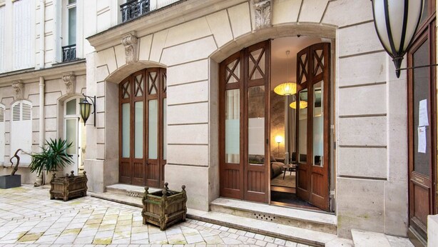 A building with large wooden doors and windows, a stone facade, and a small outdoor seating area with a lamp. - Sweett | Artois - Three Bedroom Apartment, Sleeps 6 (Paris)